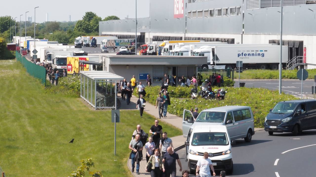 Menschen, Auto und Lkw sind an einem großen Rewe-Gebäude in Köln zu sehen.