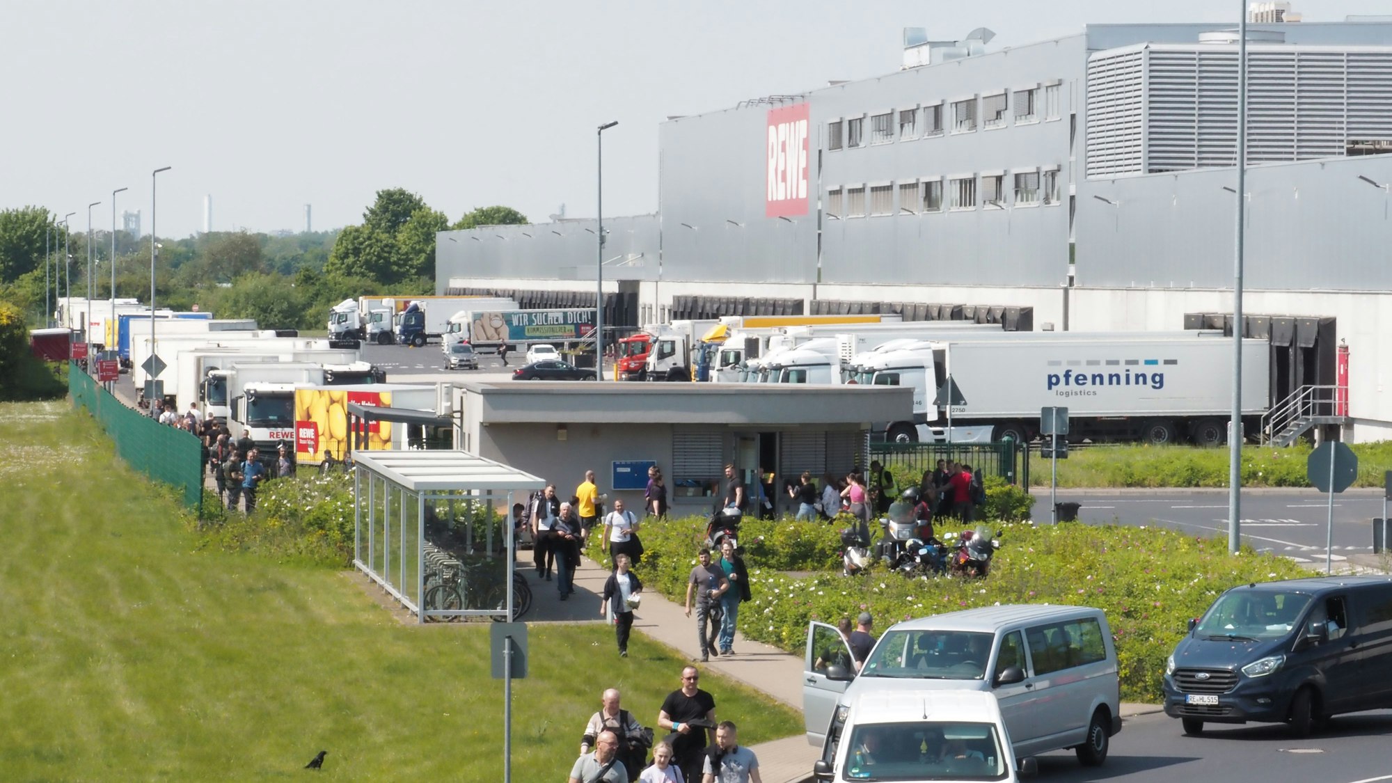Menschen, Auto und Lkw sind an einem großen Rewe-Gebäude in Köln zu sehen.