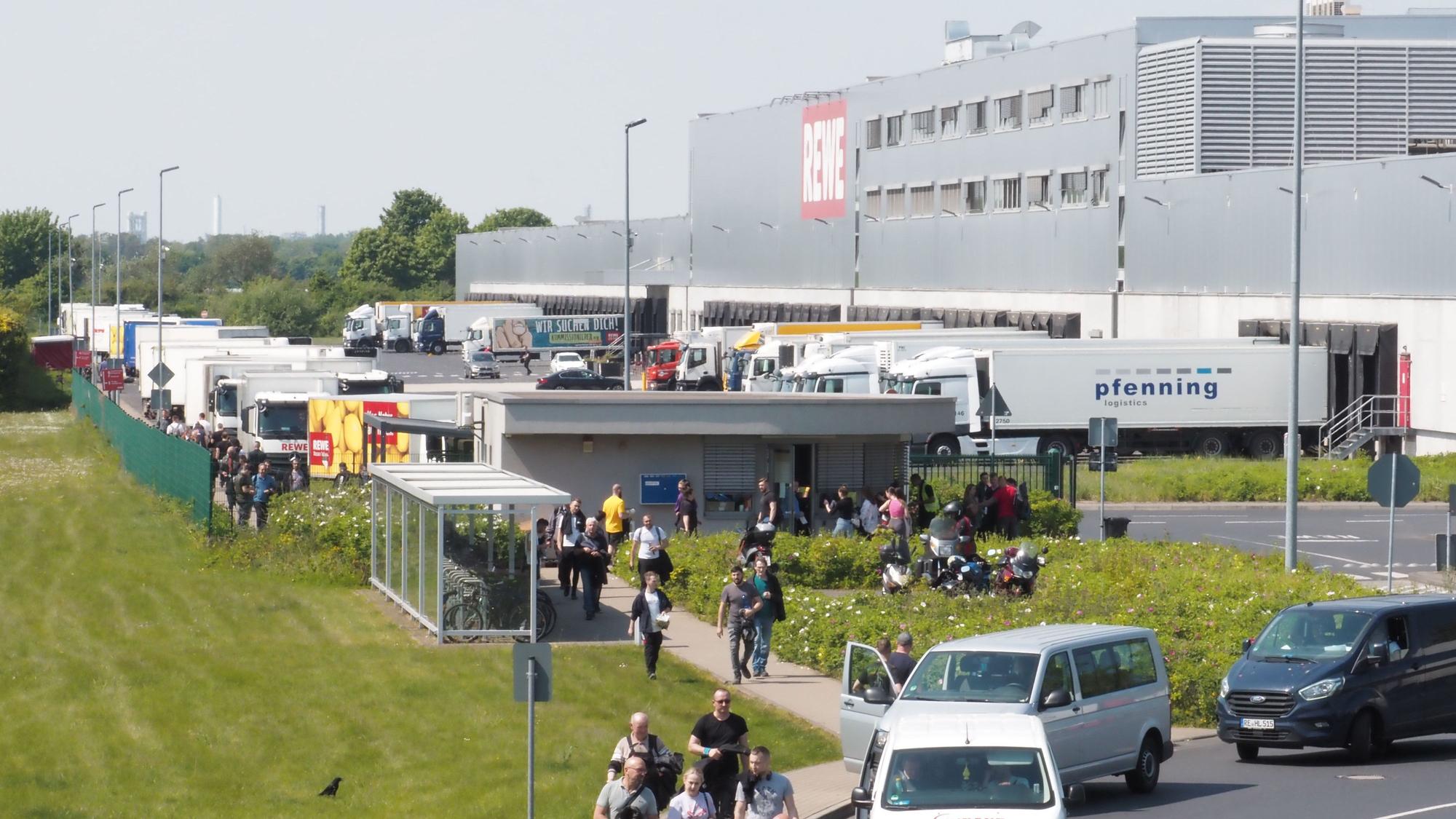 Menschen, Auto und Lkw sind an einem großen Rewe-Gebäude in Köln zu sehen.