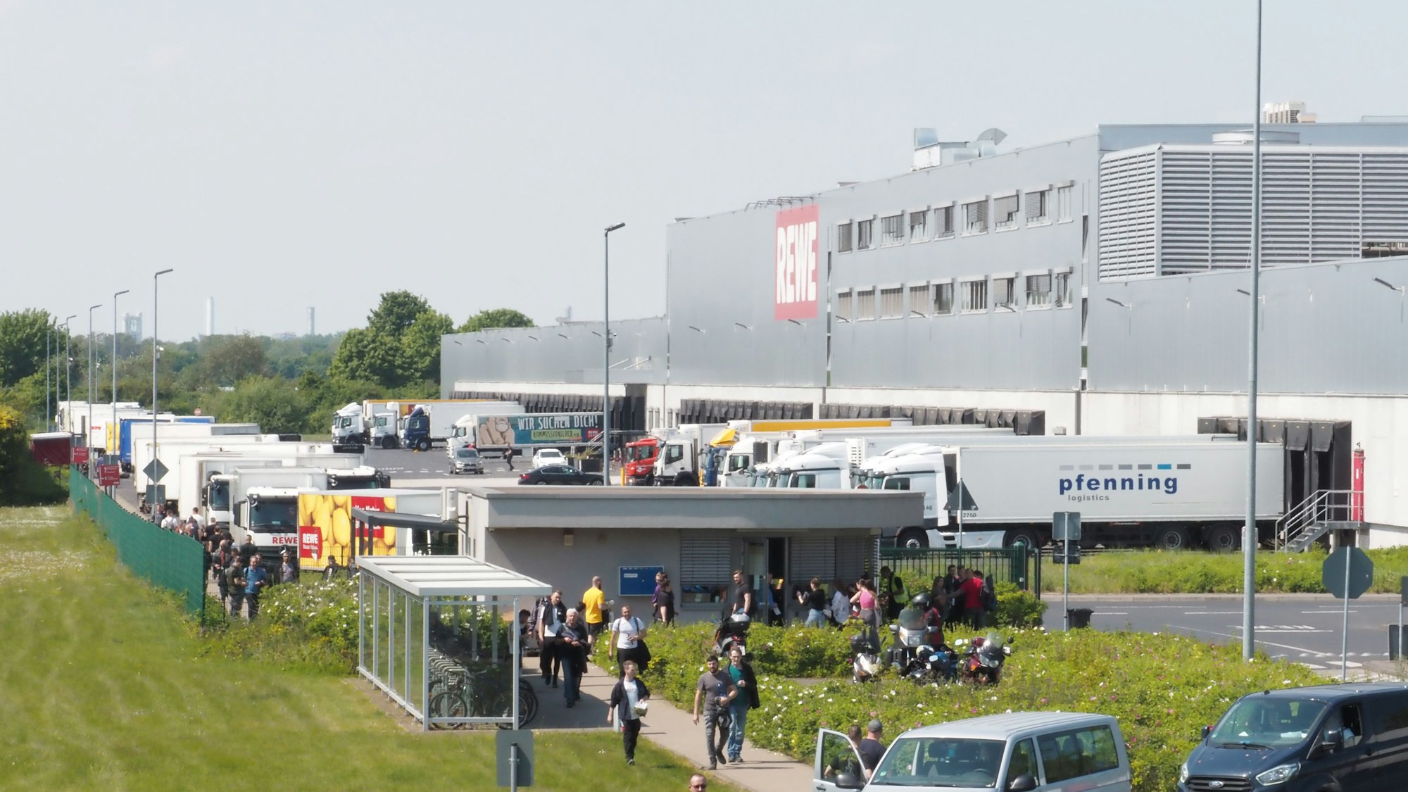 Menschen, Auto und Lkw sind an einem großen Rewe-Gebäude in Köln zu sehen.