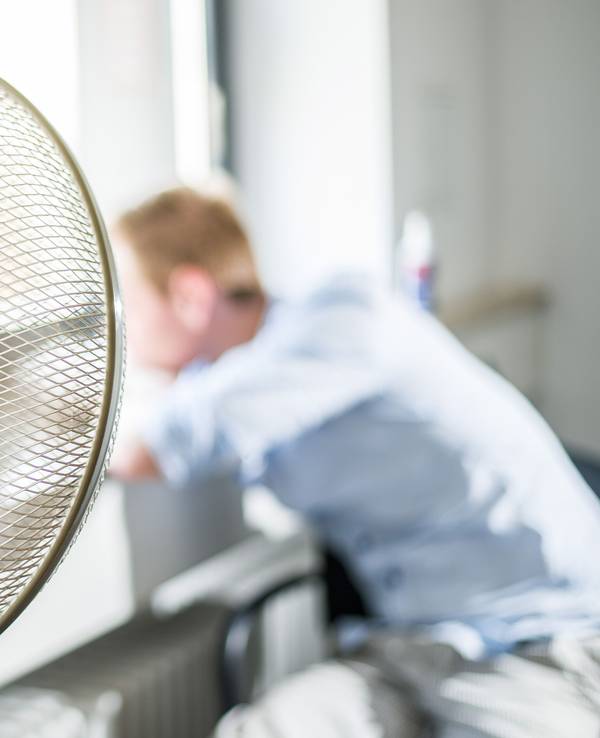 Ein Ventilator steht in einem Büro, davor sitzt ein Mann mit hellblauem Hemd.