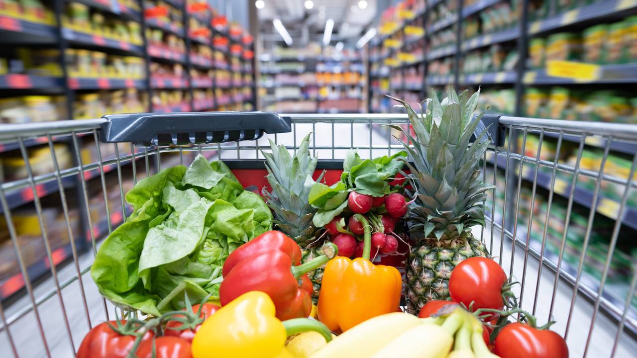 Ein Einkaufskorb mit Obst und Gemüse steht in einem Supermarkt.