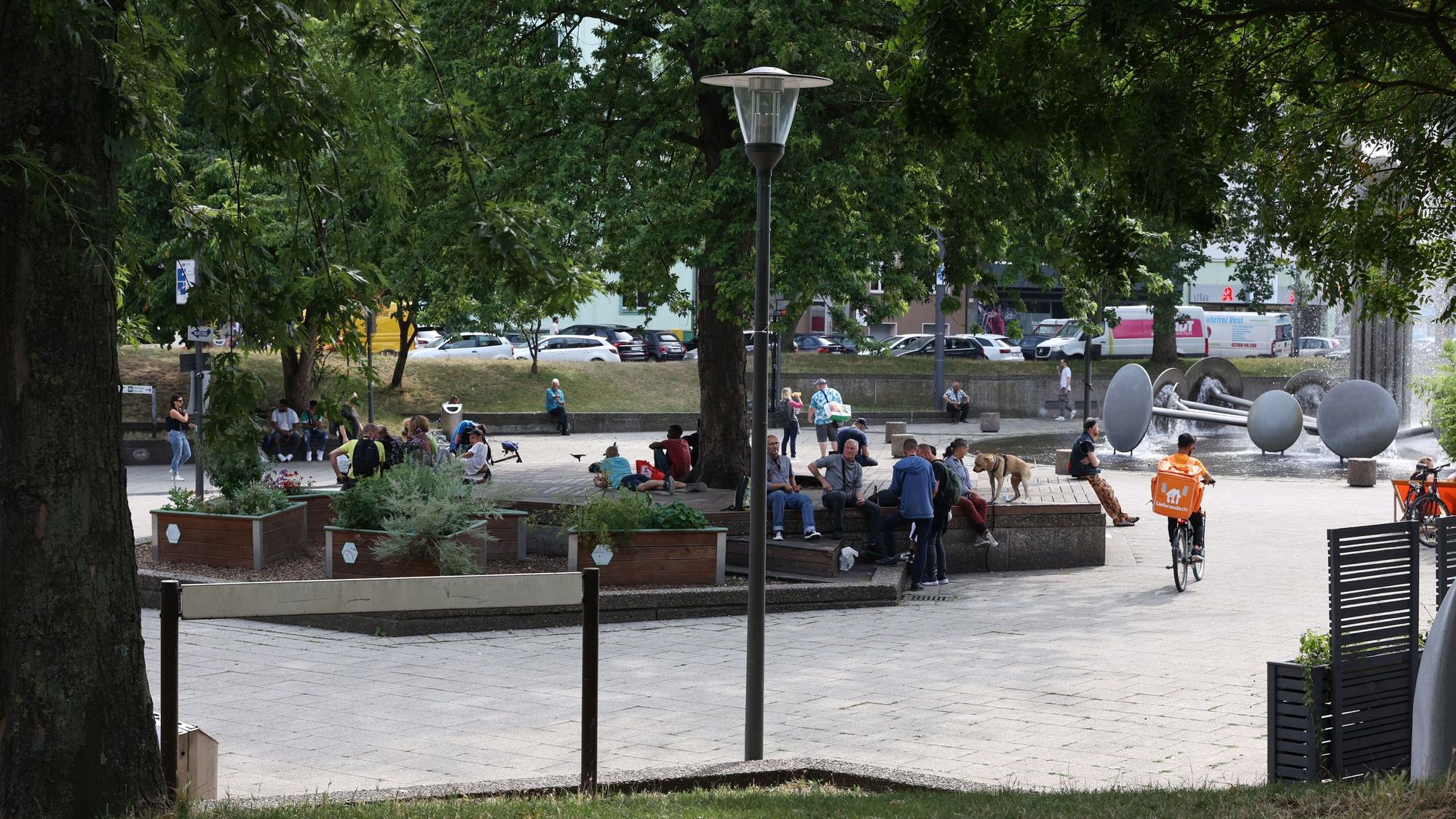 Menschen sitzen am Kölner Ebertplatz, daneben sprudelt der Brunnen.