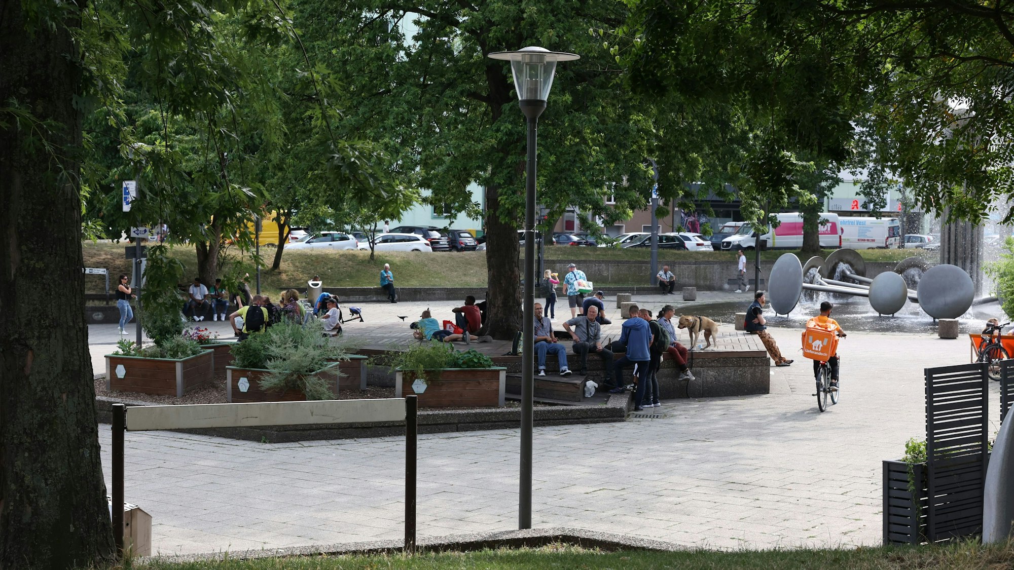 Menschen sitzen am Kölner Ebertplatz, daneben sprudelt der Brunnen.