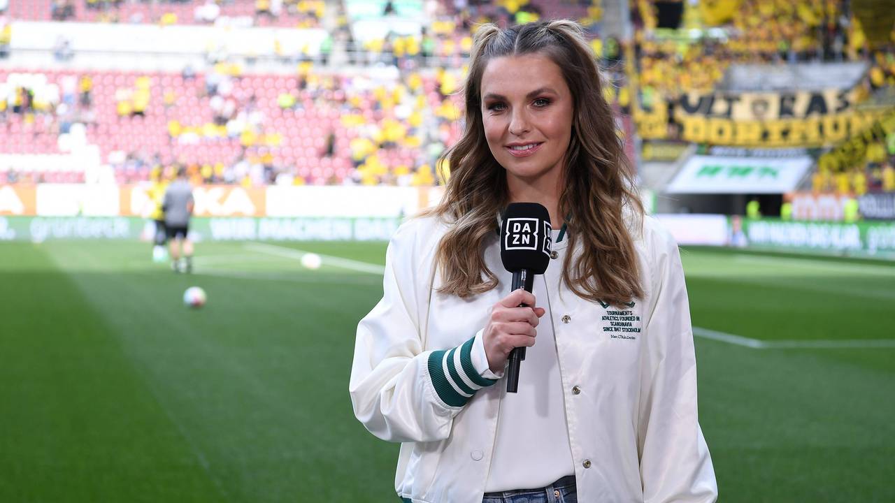Laura Wontorra steht mit DAZN-Mikrofon am Spielfeldrand.