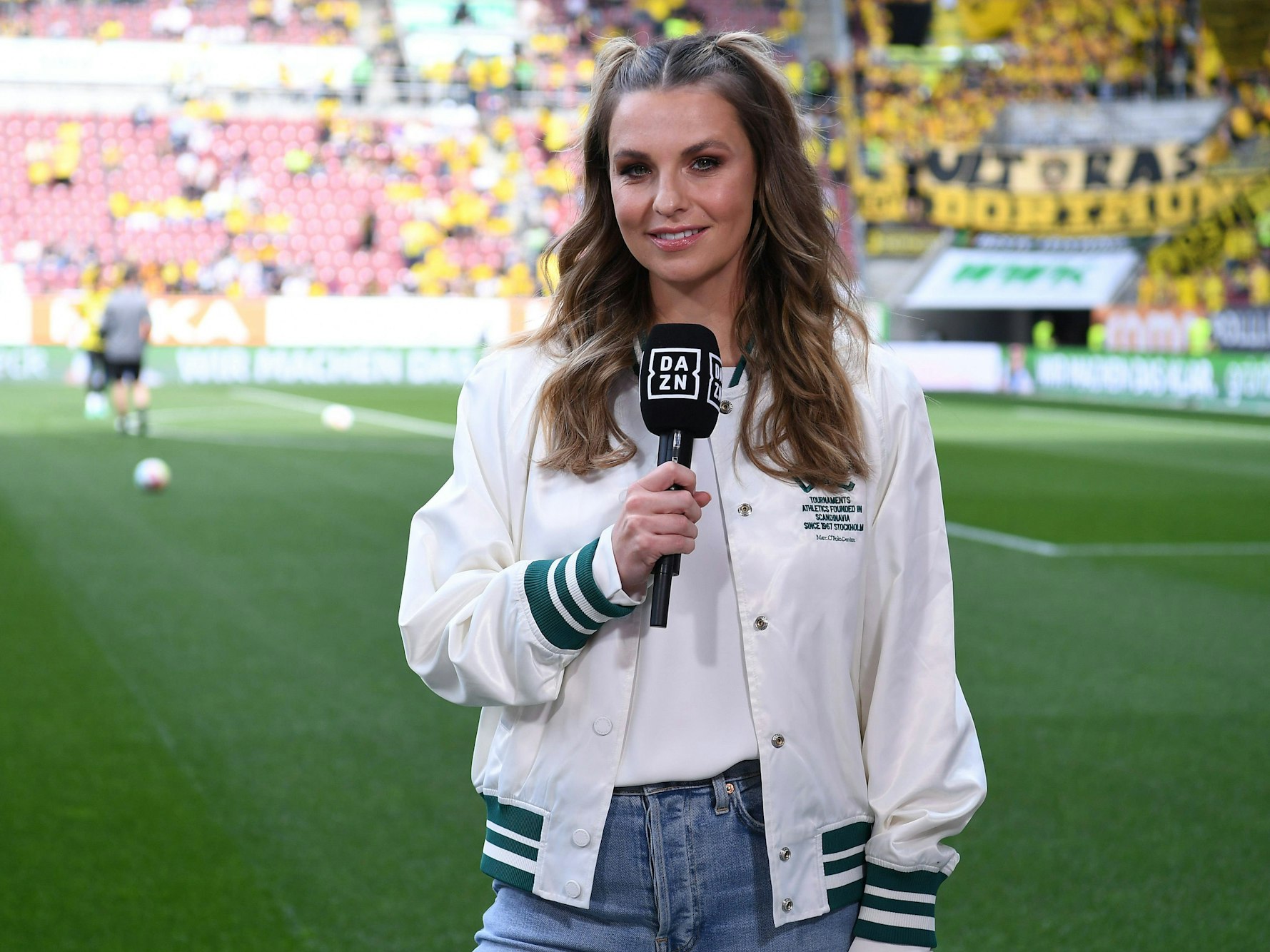 Laura Wontorra steht mit DAZN-Mikrofon am Spielfeldrand.