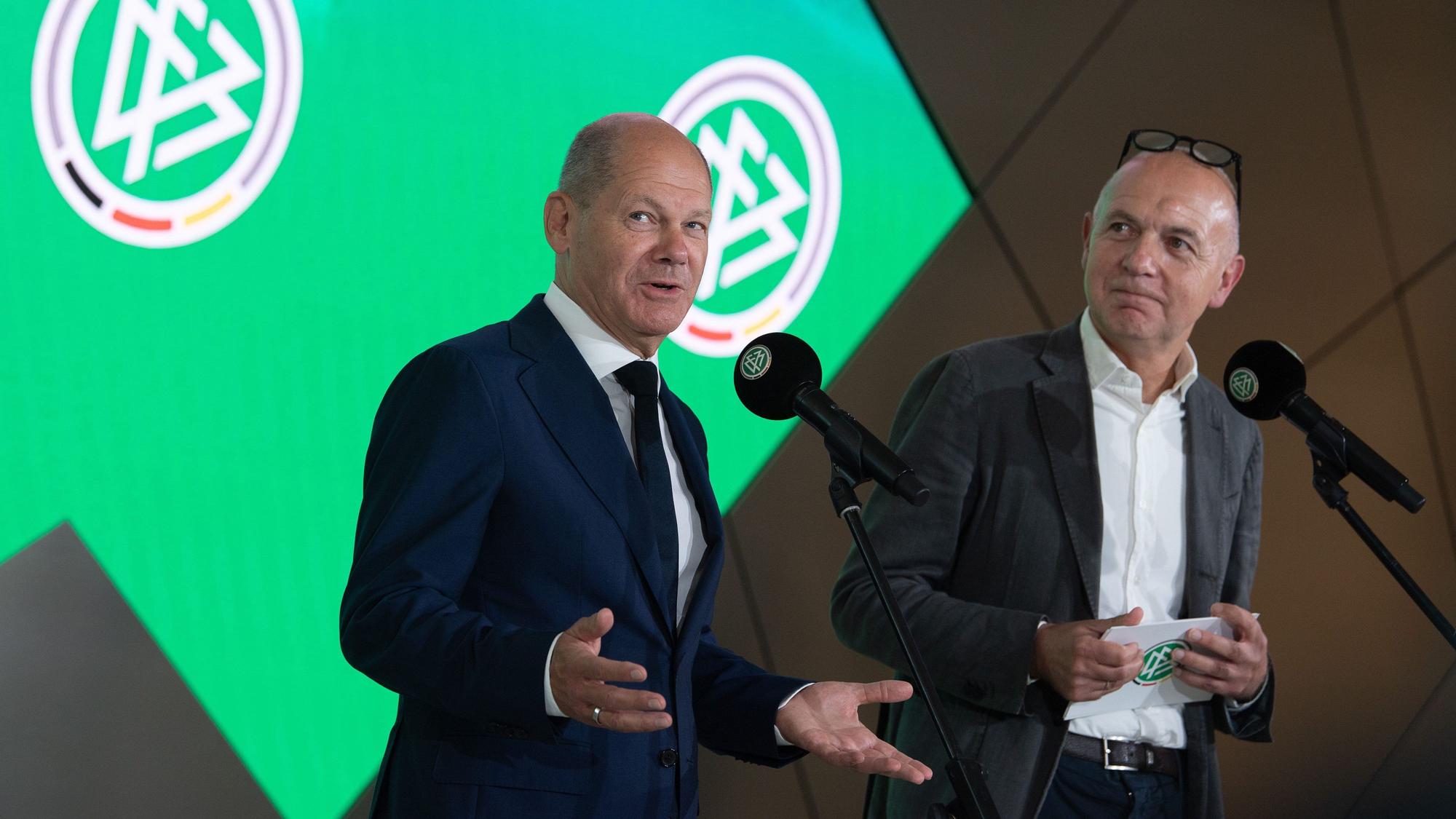 Bundeskanzler Olaf Scholz spricht neben Bernd Neuendorf.