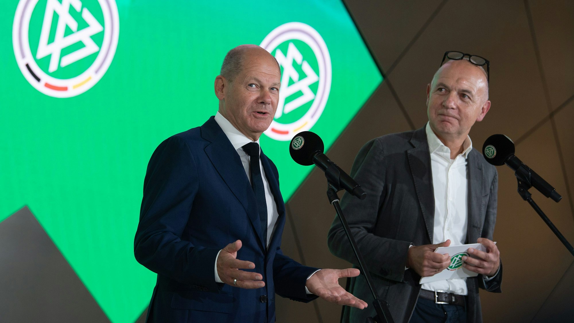 Bundeskanzler Olaf Scholz spricht neben Bernd Neuendorf.