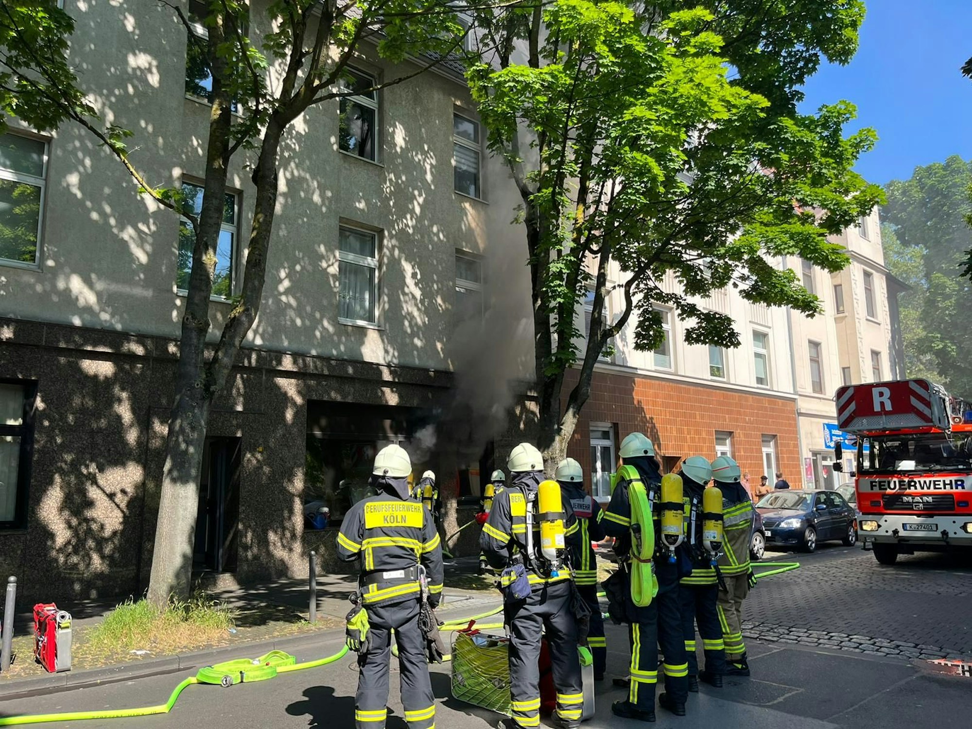 Feuerwehrleute stehen vor einem brennenden Bestattungsunternehmen in Köln-Humboldt.