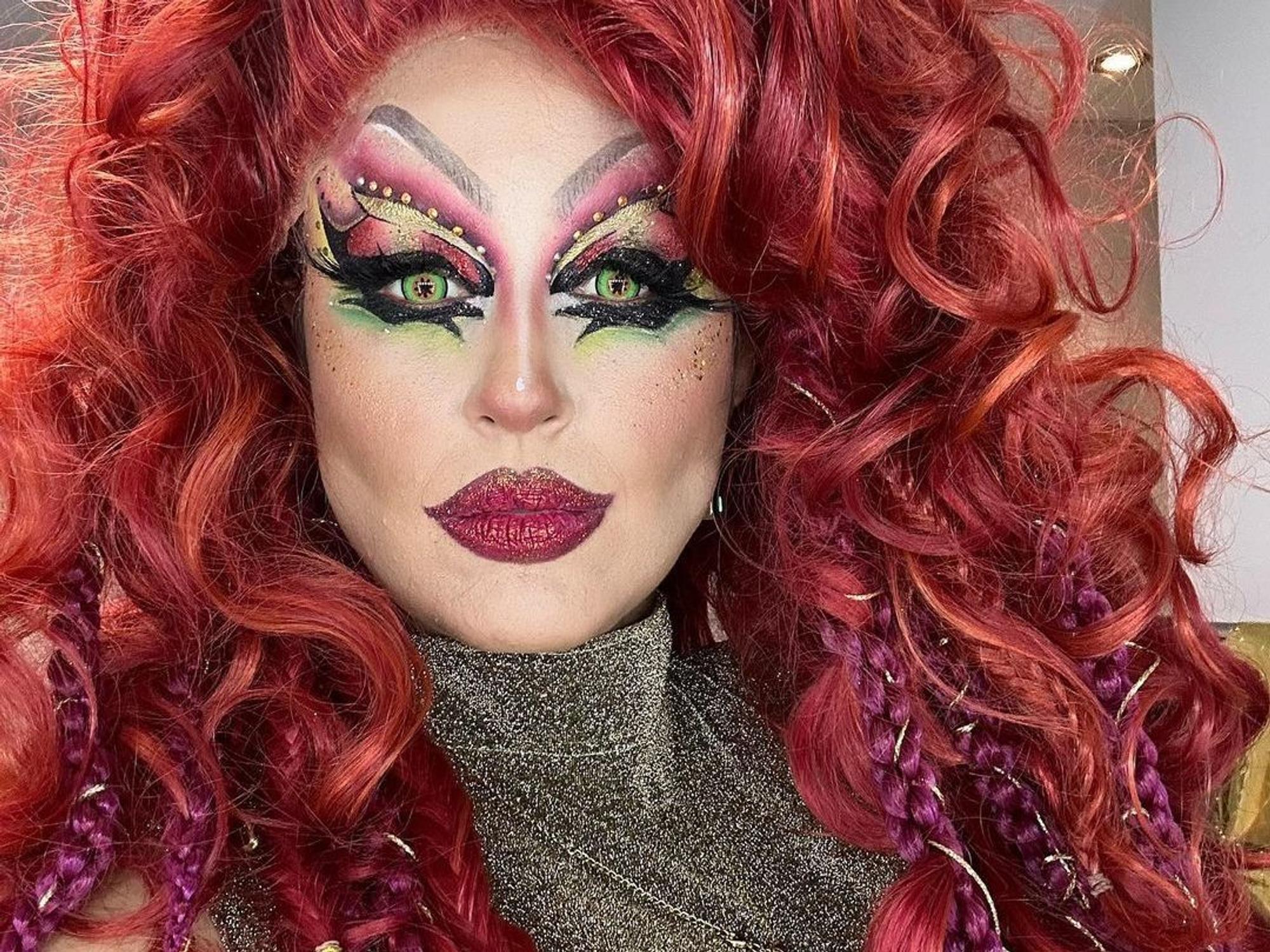 Moderatorin Nina Moghaddam als Drag-Queen mit buntem Make-up und roter Perücke bei der Show „Viva la Diva – Wer ist die Queen?“.