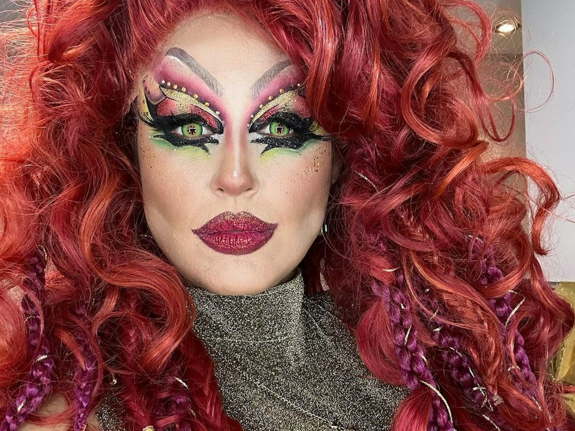 Moderatorin Nina Moghaddam als Drag-Queen mit buntem Make-up und roter Perücke bei der Show „Viva la Diva – Wer ist die Queen?“.