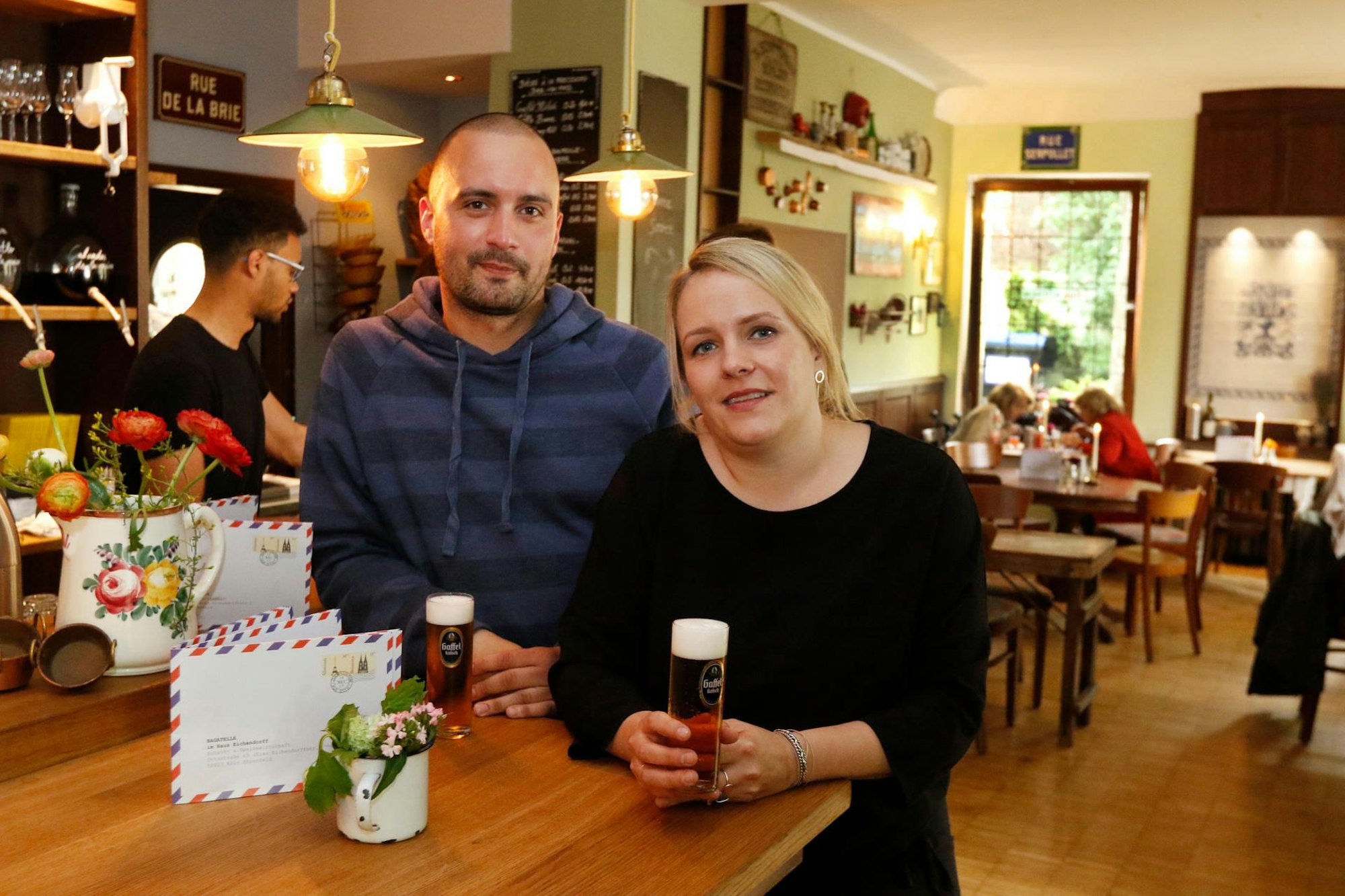 Reja und Daniel Rabe schauen in die Kamera und halten ein Kölsch in der Hand.