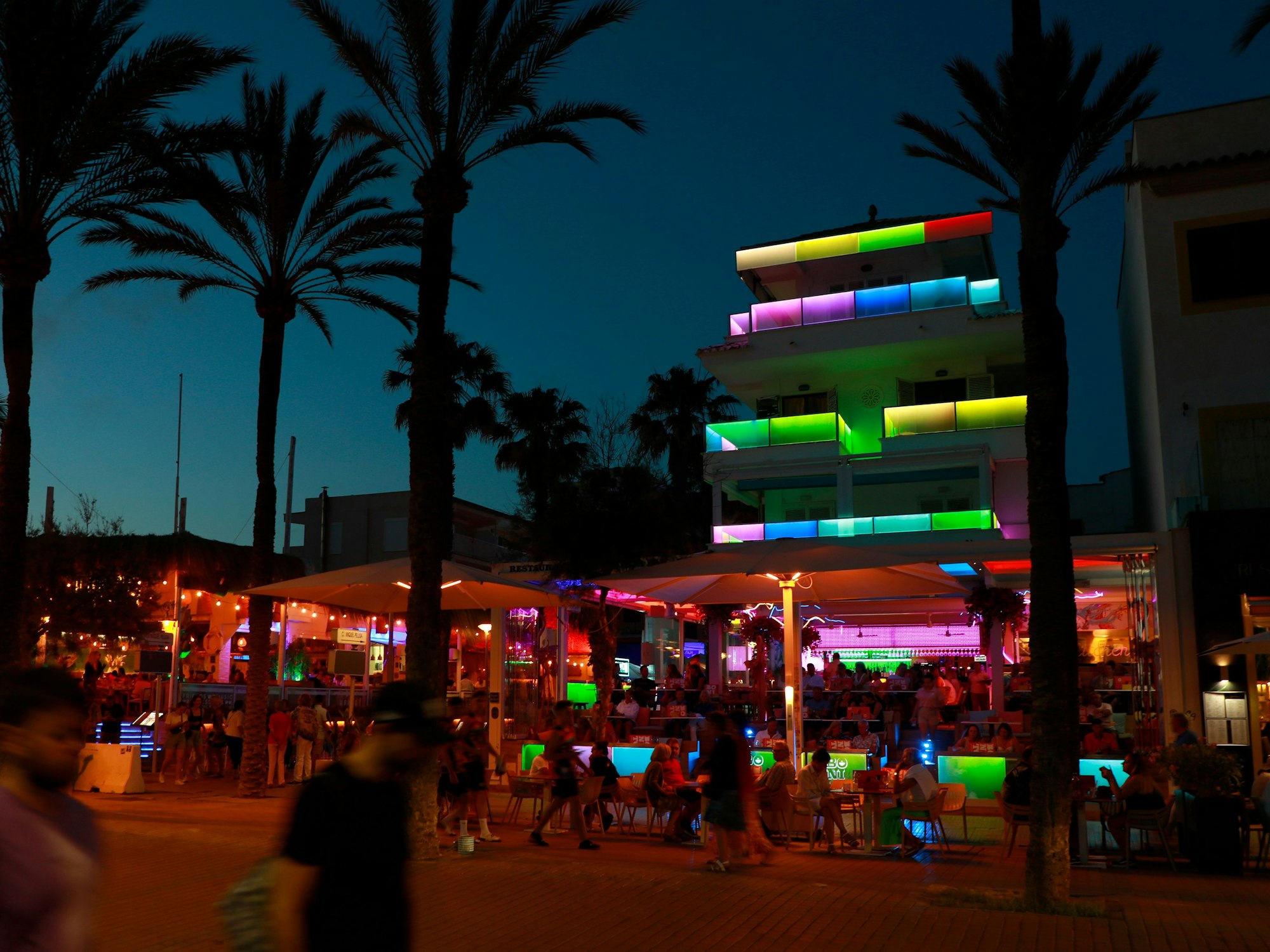 Menschen spazieren auf der Bierstraße am Strand von Arenal an vollen Bars und Lokalen vorbei.