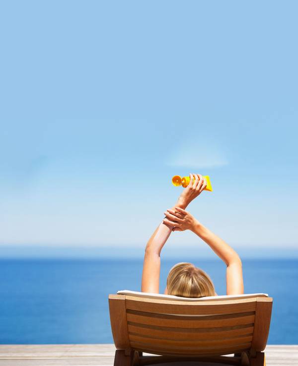Relaxte Frau am Strand mit Sonnencreme-Tube in der Hand