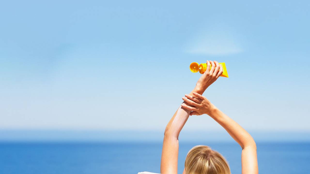 Relaxte Frau am Strand mit Sonnencreme-Tube in der Hand