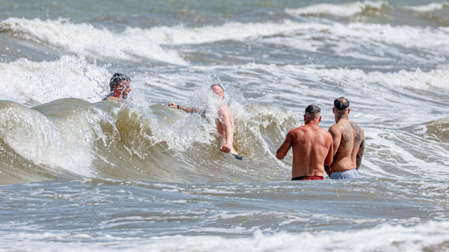 Vier Männer baden am 10. Juni 2023 in starker Brandung vor dem Timmendorfer Strand.