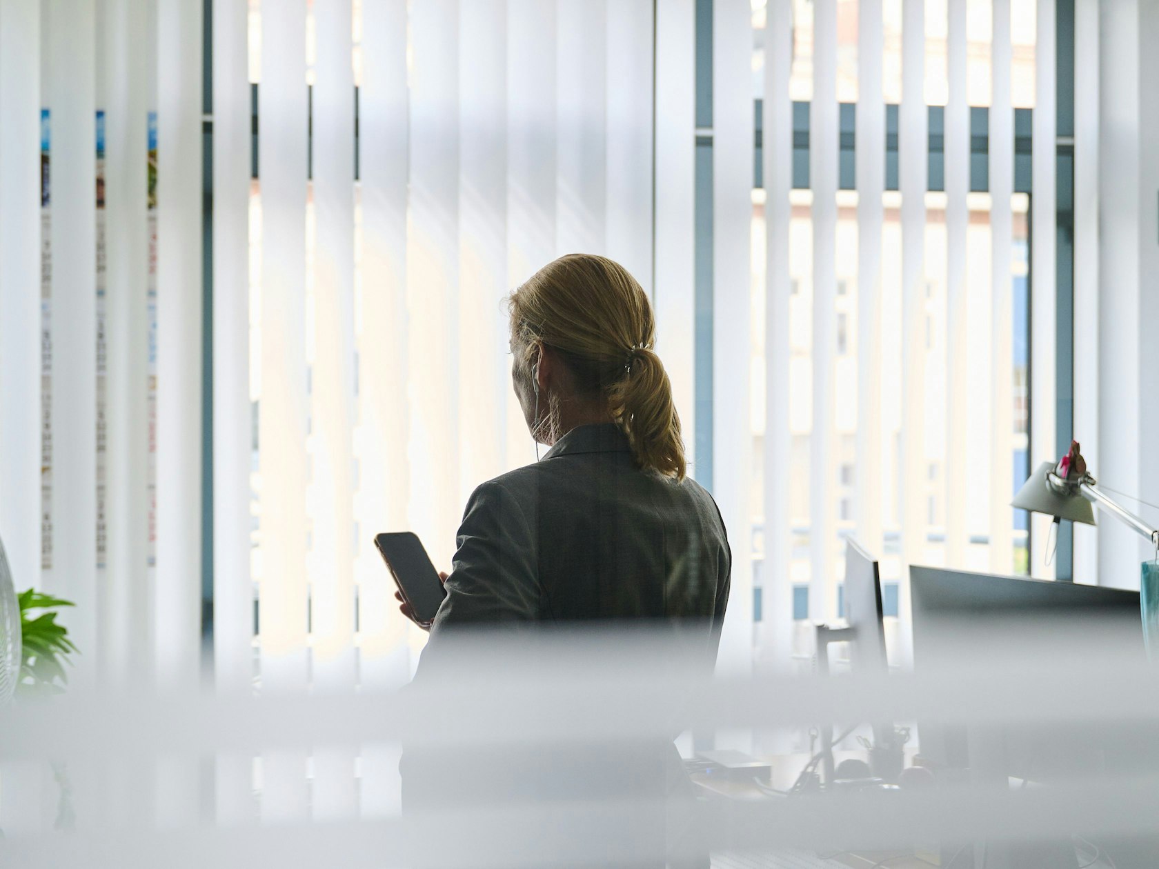 Eine Frau steht in einem Bürozimmer am Fenster und telefoniert über ein Headset. (gestellte Szene)