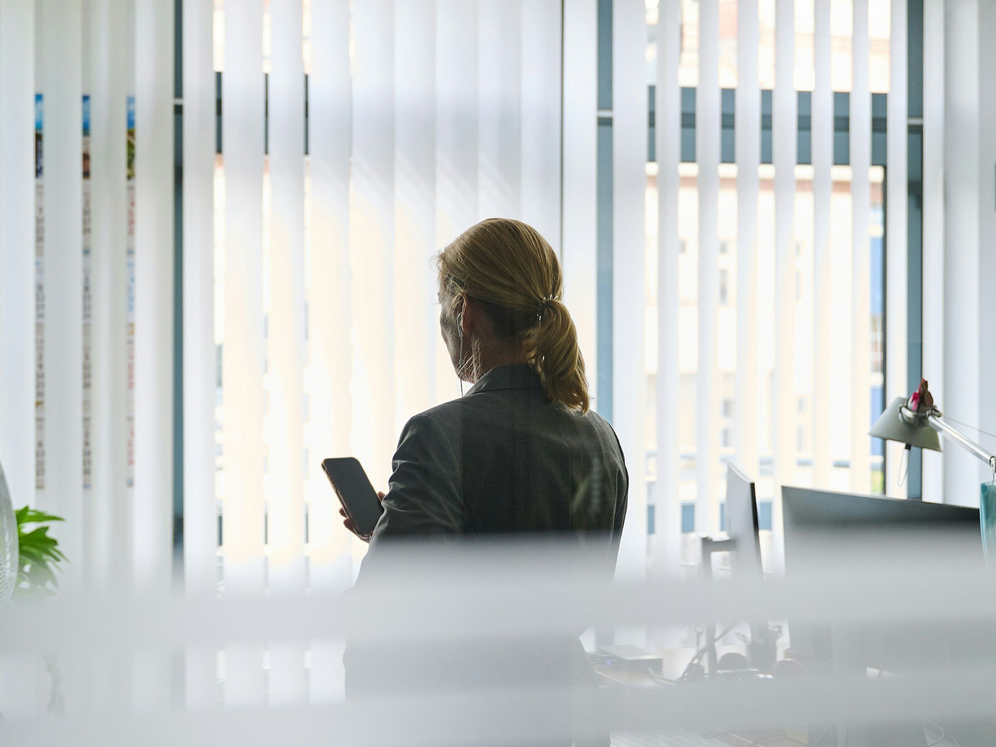 Eine Frau steht in einem Bürozimmer am Fenster und telefoniert über ein Headset. (gestellte Szene)