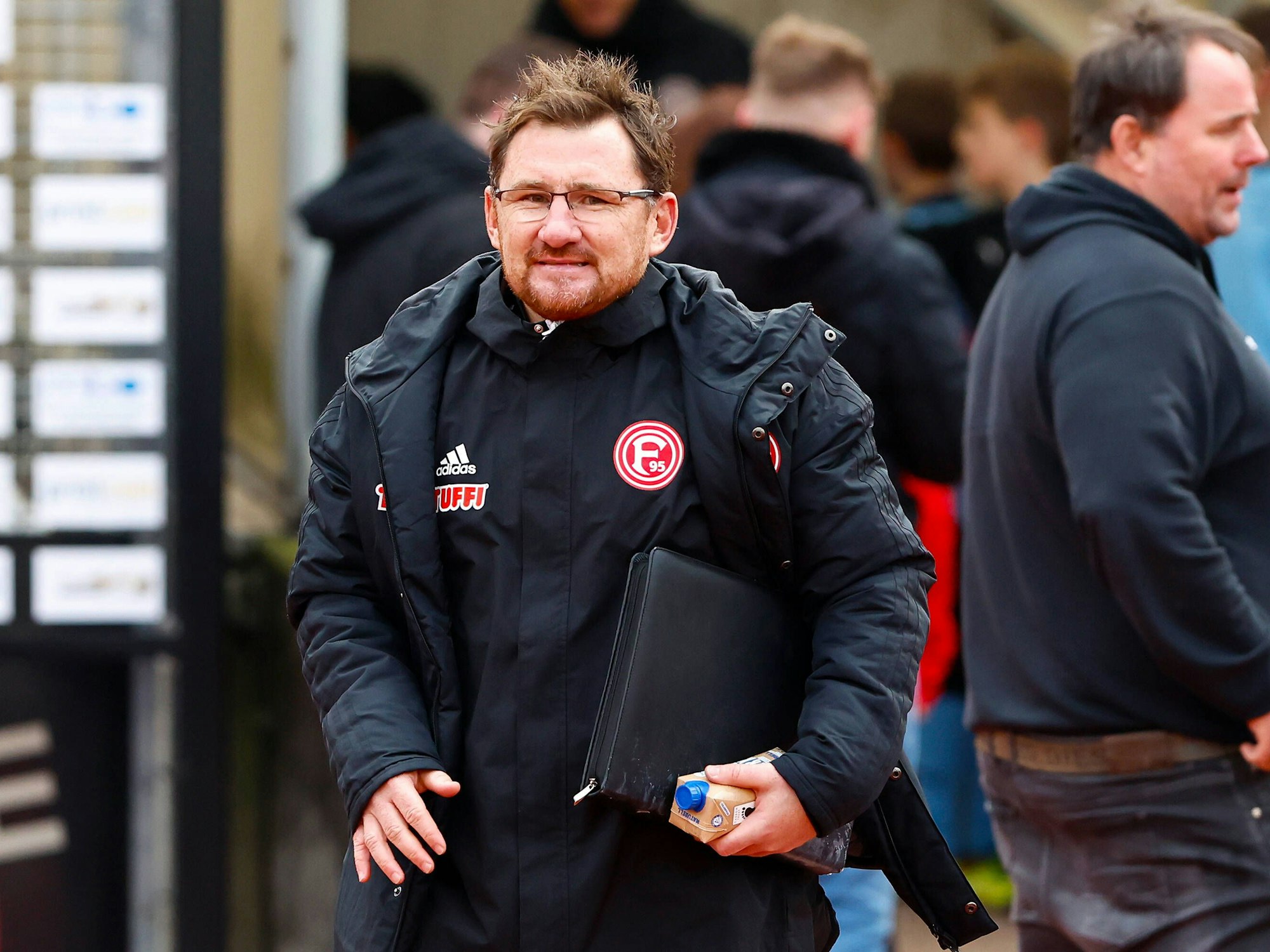 Fortuna Düsseldorfs Co-Trainer Paul Freier steht mit Mappe unterm Arm in Wattenscheid auf dem Platz.