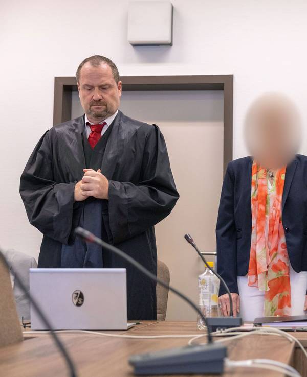 Eine Frau steht an der Anklagebank zwischen zwei Anwälten.