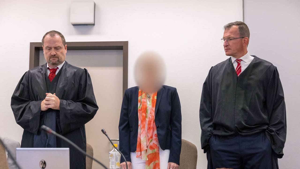 Eine Frau steht an der Anklagebank zwischen zwei Anwälten.
