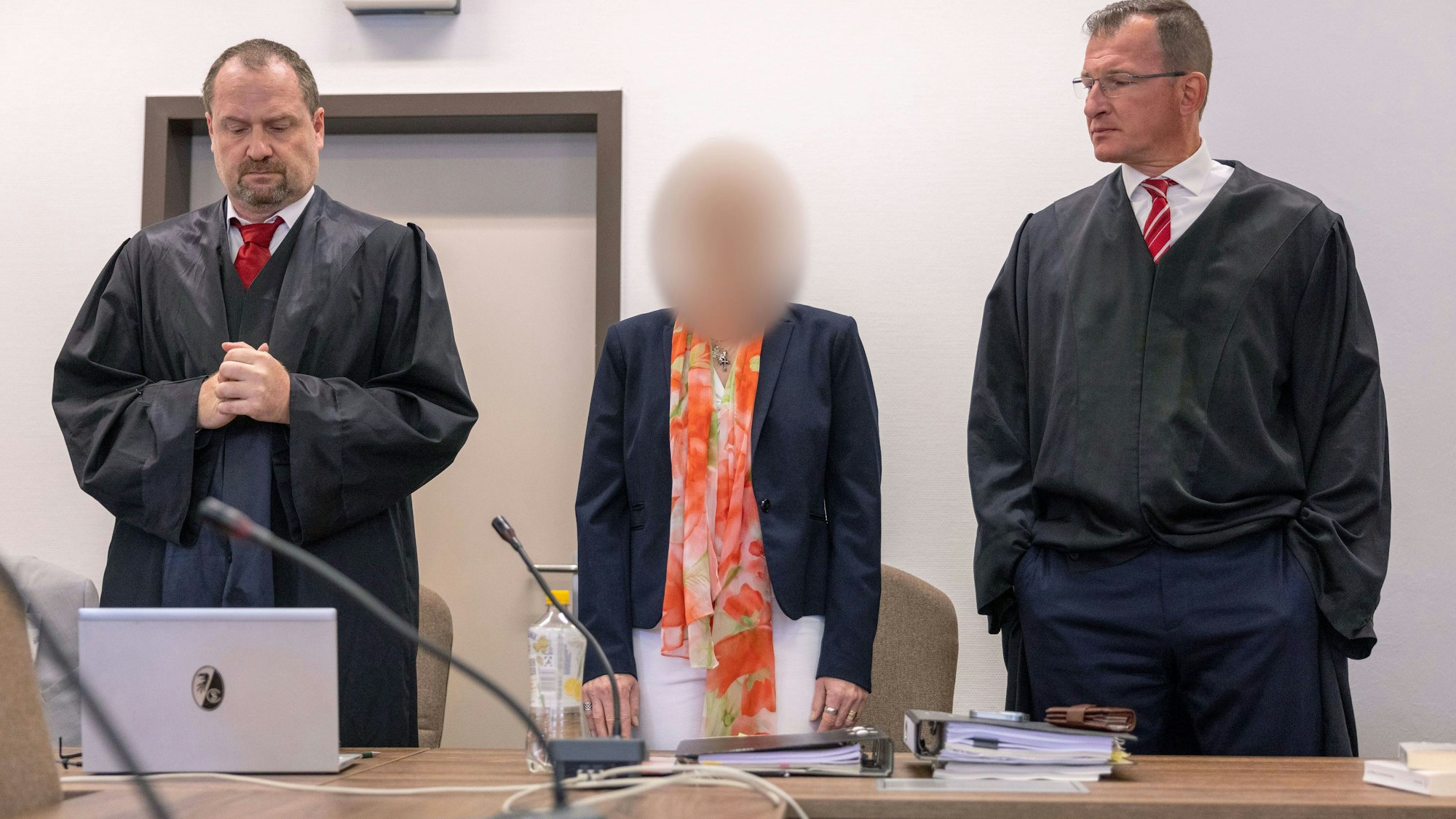 Eine Frau steht an der Anklagebank zwischen zwei Anwälten.