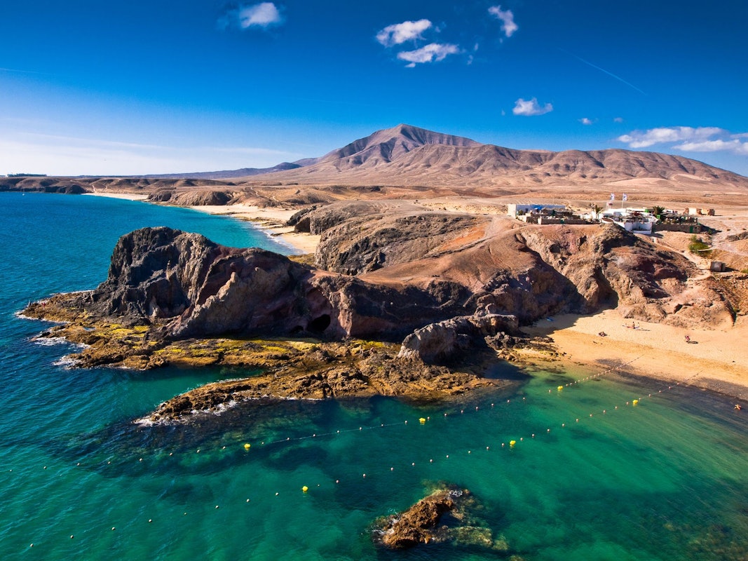 Braune Felsen ragen in türkisfarbenes Meer am Strand.