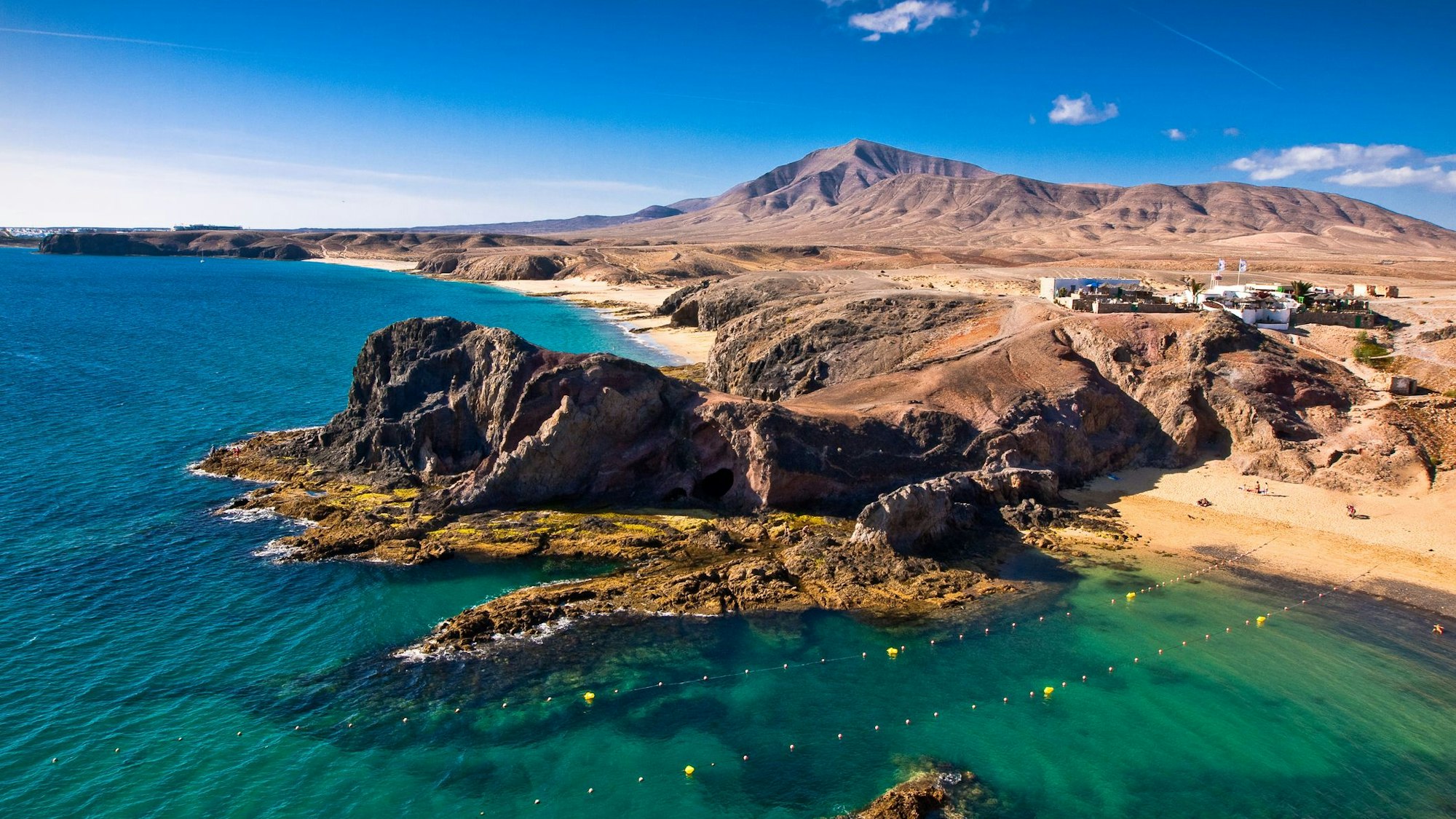 Braune Felsen ragen in türkisfarbenes Meer am Strand.