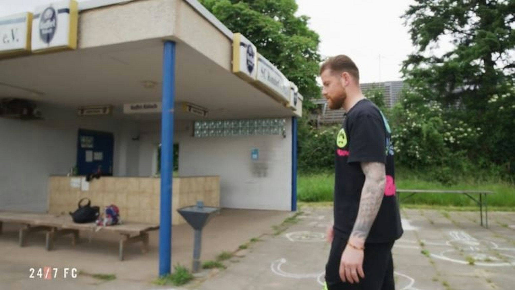 Timo Horn geht auf der Anlage des SC Rondorf umher, im Hintergrund ist das Vereinsheim zu sehen.