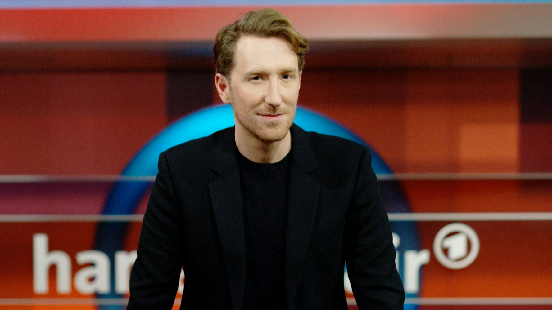 Louis Klamroth schaut in die Kamera. Hinter seinem Rücken sind noch Teile des „Hart aber fair“-Schrifzugs zu erkennen.