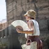 Eine Frau schützt sich mit einem Hut und einem Fächer vor der Sonne und der Hitze.