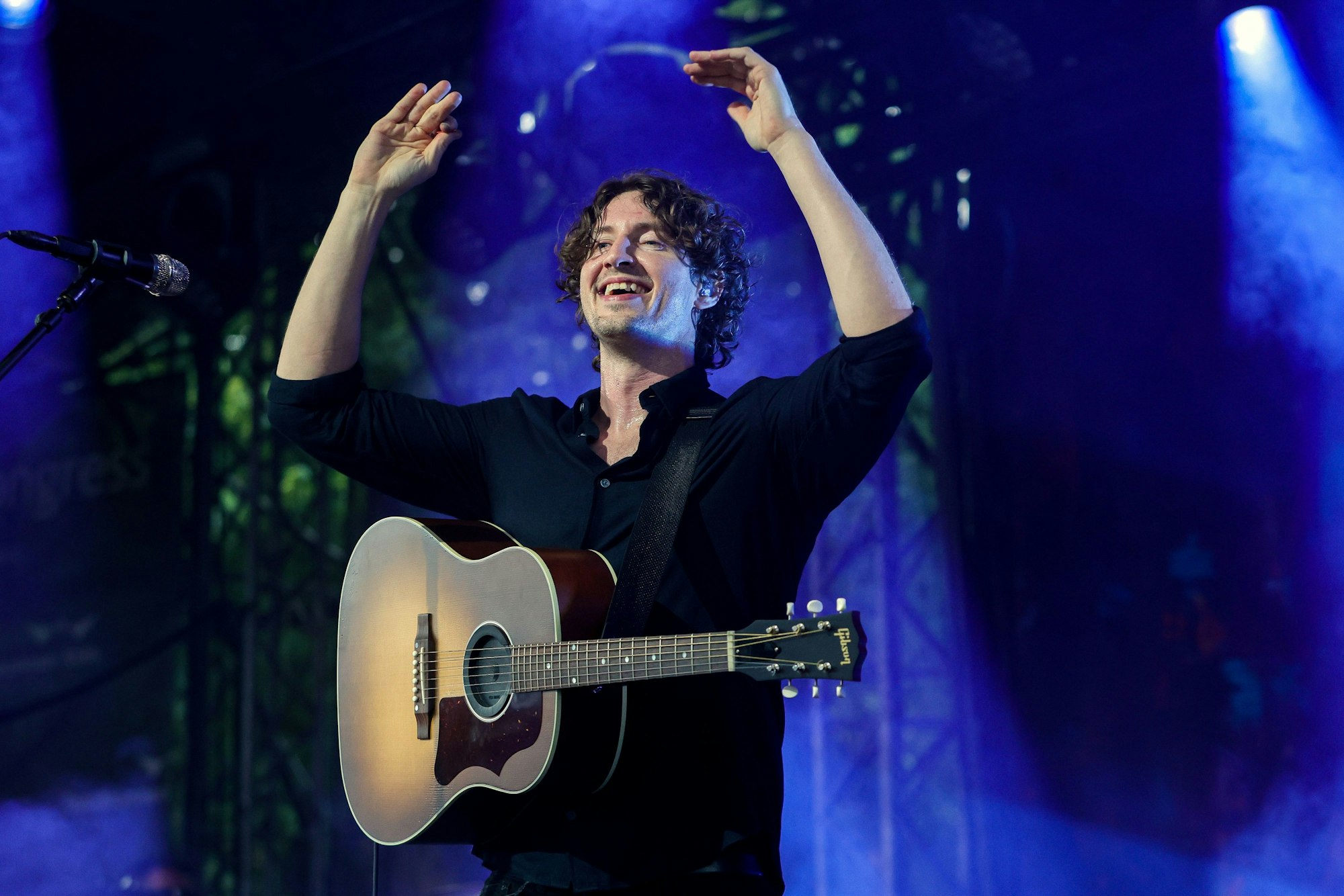 Dean Lewis steht auf der Bühne, reckt die Arme in die Höhe und lacht.