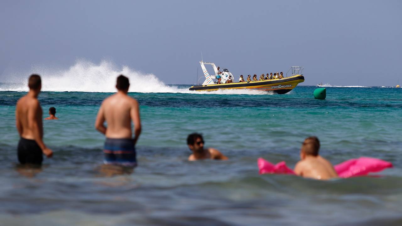Eine Schlauchboot mit Touristen fährt neben den Badegästen am Strand von El Arenal in Palma de Mallorca, einem der Hauptziele für deutsche und niederländische Touristen während der Sommersaison.