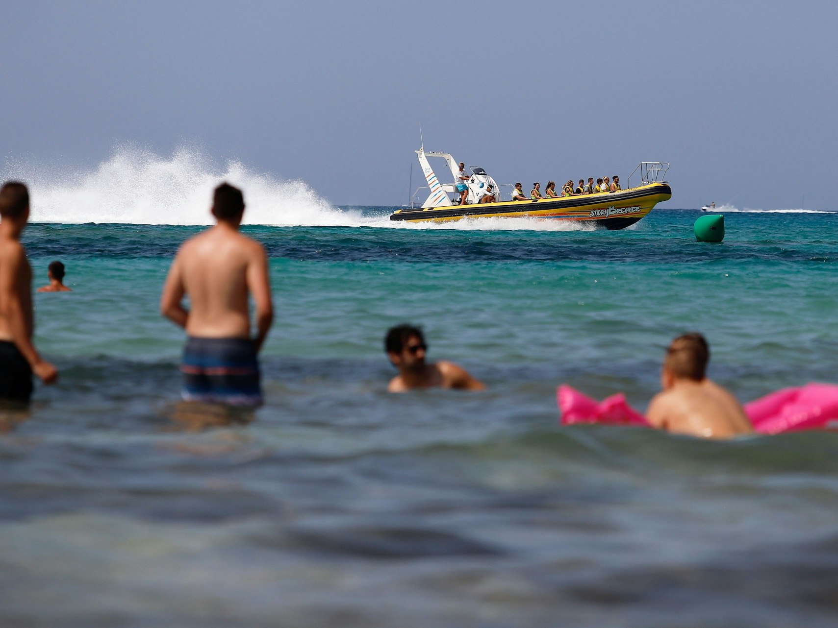 Eine Schlauchboot mit Touristen fährt neben den Badegästen am Strand von El Arenal in Palma de Mallorca, einem der Hauptziele für deutsche und niederländische Touristen während der Sommersaison.