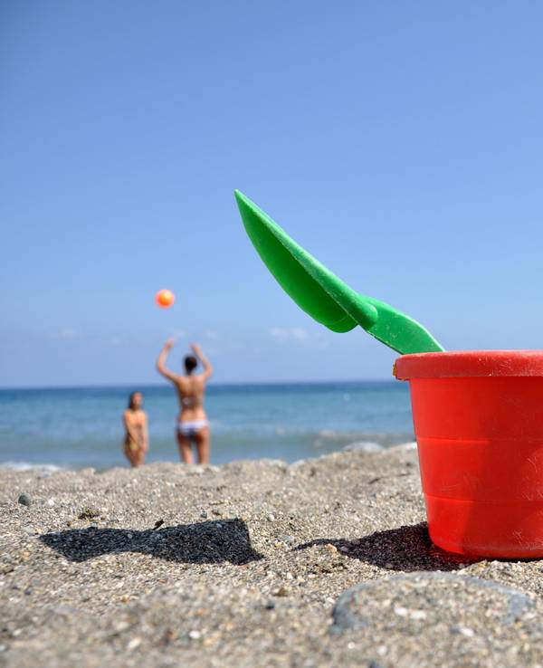 Strandspielzeug steht im Sand, im Hintergrund spielen zwei Frauen Volleyball.