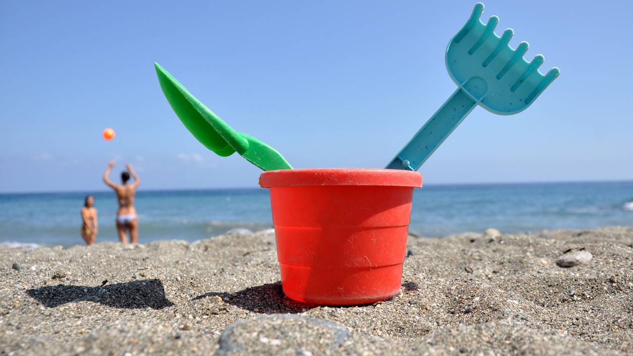 Strandspielzeug steht im Sand, im Hintergrund spielen zwei Frauen Volleyball.