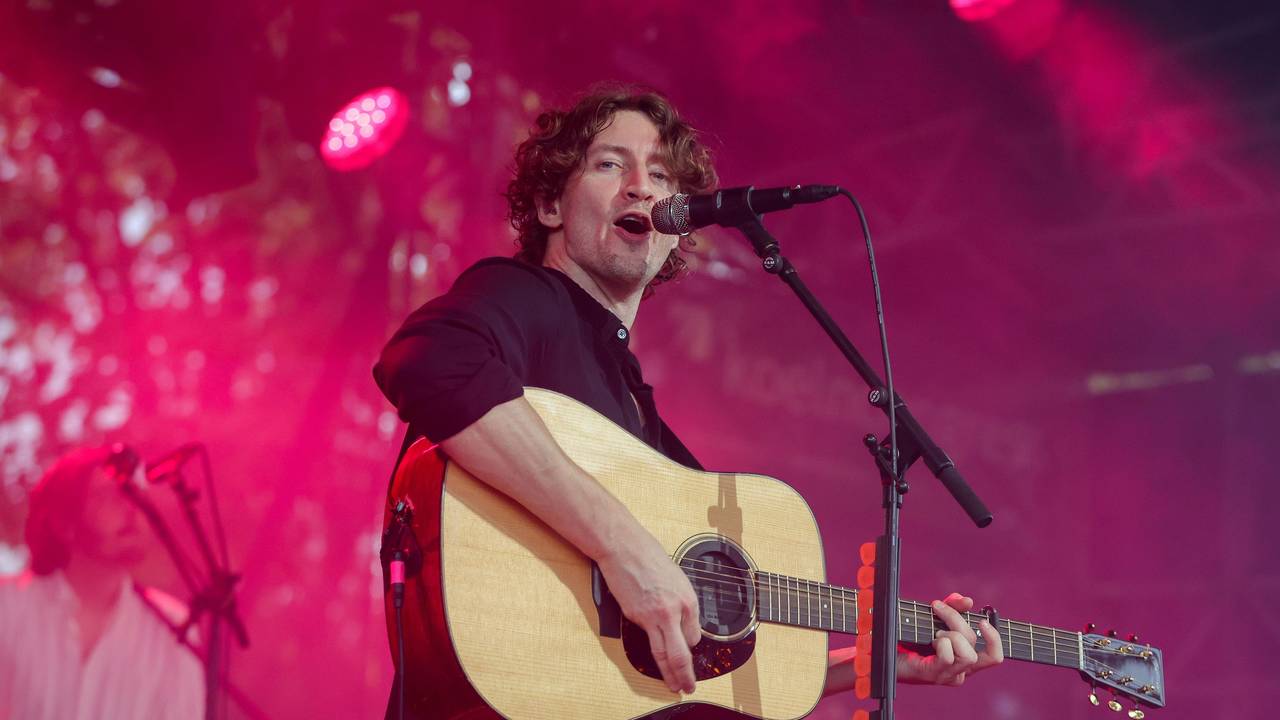 Dean Lewis steht mit seiner Gitarre auf der Bühne und singt.