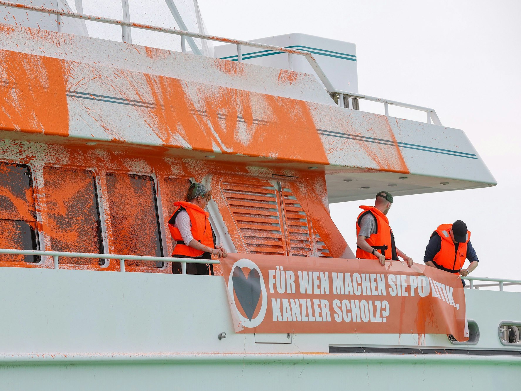 Teilnehmende einer Protestaktion stehen am 20. Juni 2023 mit Transparenten auf einer Jacht im Hafen von Neustadt in Holstein. Auf einem Transparent ist die Aufschrift „Für wen machen Sie Politik, Kanzler Scholz?“ zu lesen.