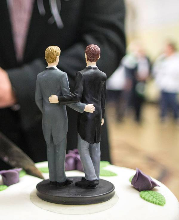 Zwei Männer schneiden nach ihrer Eheschließung im Rathaus eine Hochzeitstorte an.