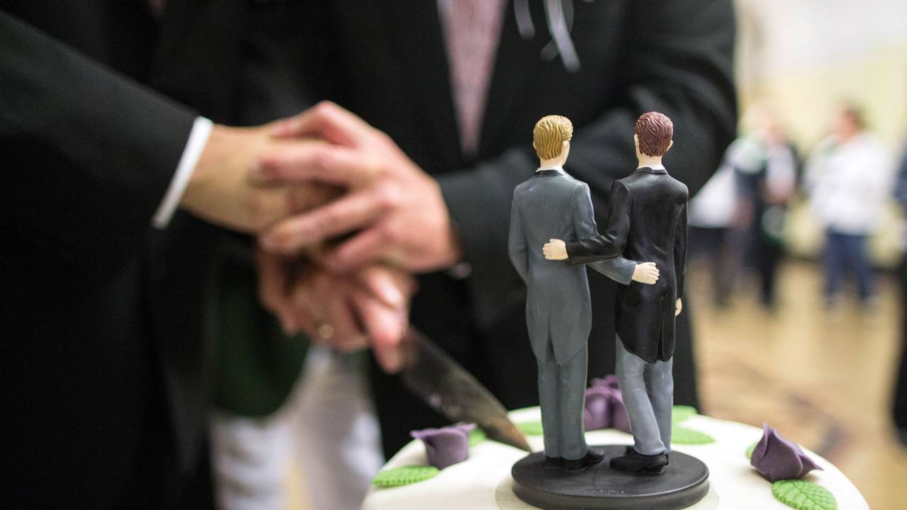 Zwei Männer schneiden nach ihrer Eheschließung im Rathaus eine Hochzeitstorte an.