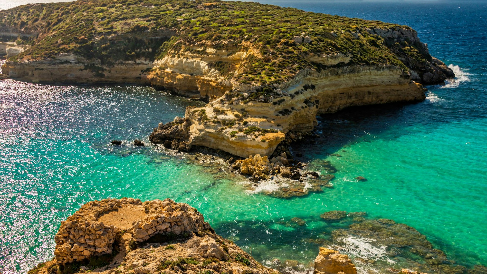 Braune Klippen treffen auf ein grün-türkisenes Meer.