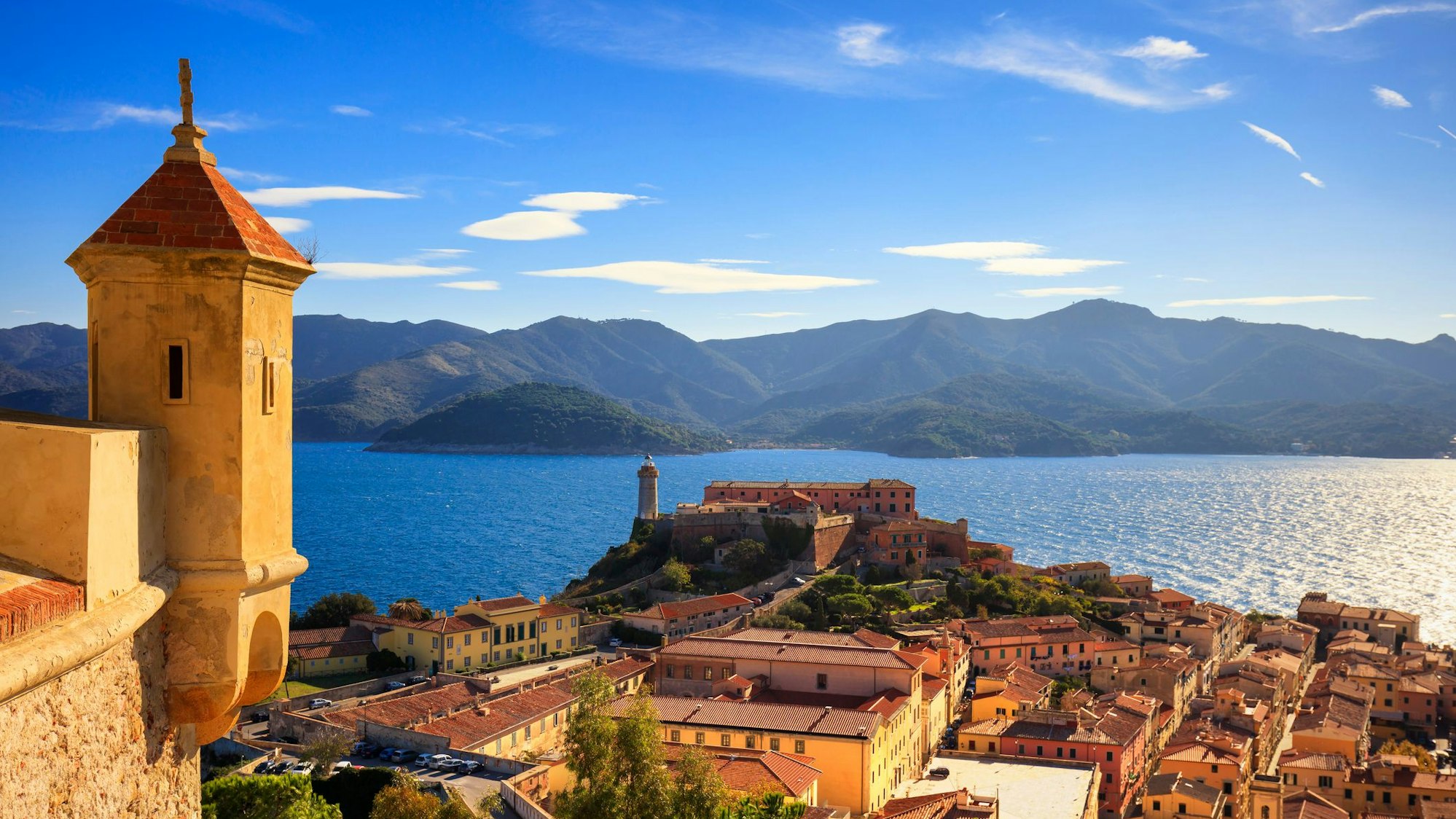 Eine gelbe Stadt vor Meer und Bergen.