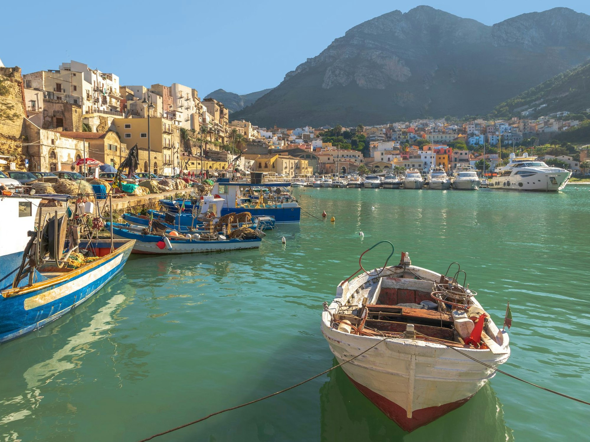 Ein Boot treibt in einem Hafen vor bergiger Kulisse.