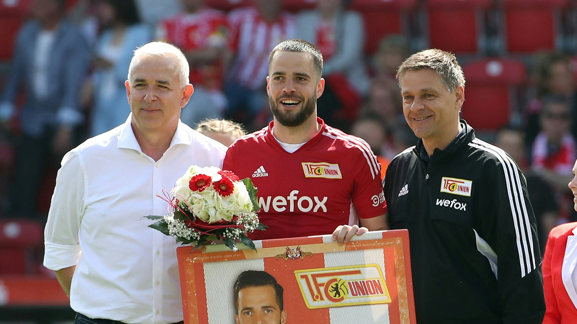 Union-Präsident Dirk Zingler, Spieler Niko Gießelmann und Sportdirektor Oliver Ruhnert stehen nebeneinander auf dem Rasen.