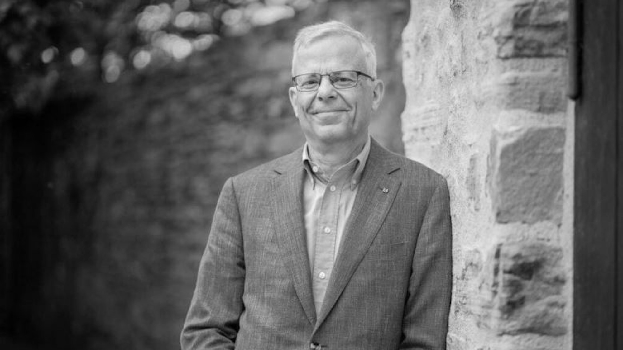 Der FDP-Fraktionsvorsitzende Jörg Krell ist gestorben. Auf dem Schwarz-weiß-Foto lehnt er an einer Steinwand.