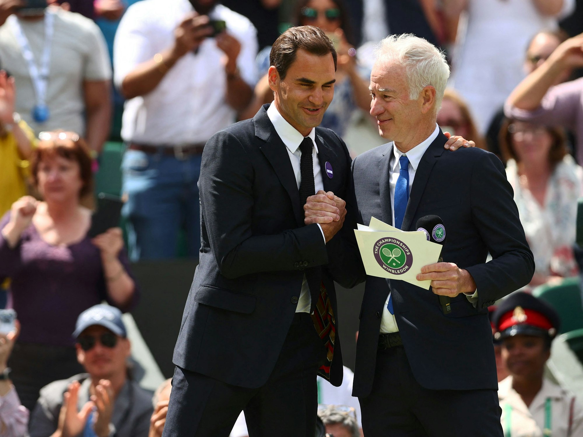 Die beiden ehemaligen Tennisstars Roger Federer (l.) und John McEnroe (r.) geben sich im Rahmen des Tennisturniers vom Wimbledon die Hand.