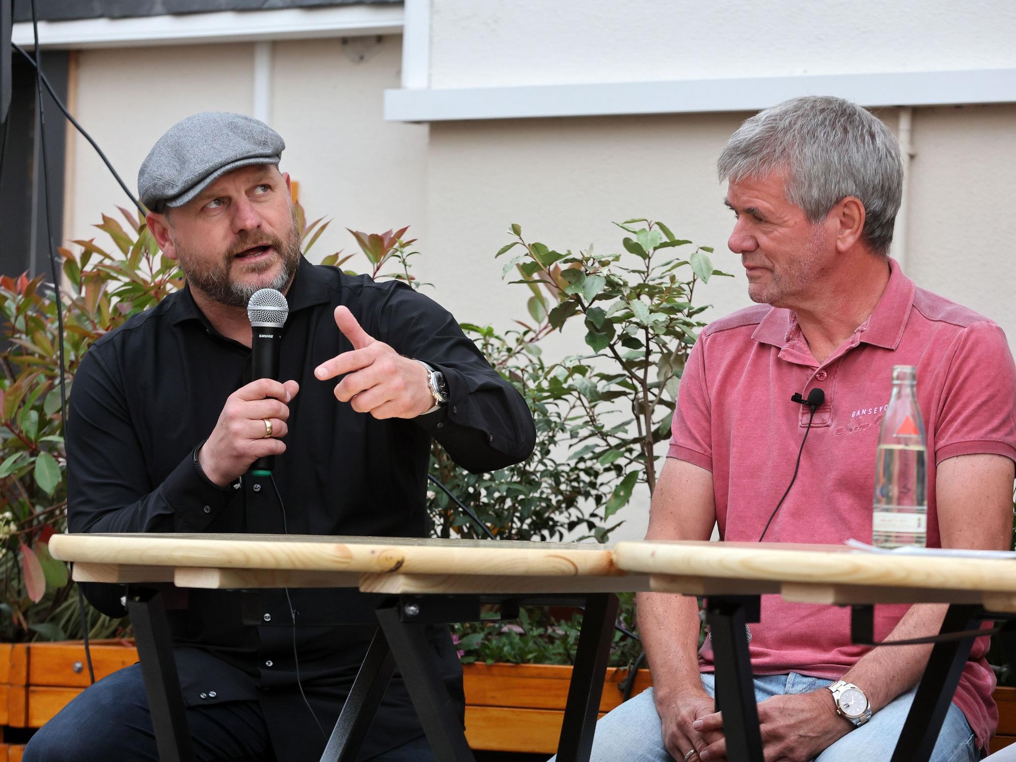 Steffen Baumgart sitzt mit Mikrofon neben Friedhelm Funkel.