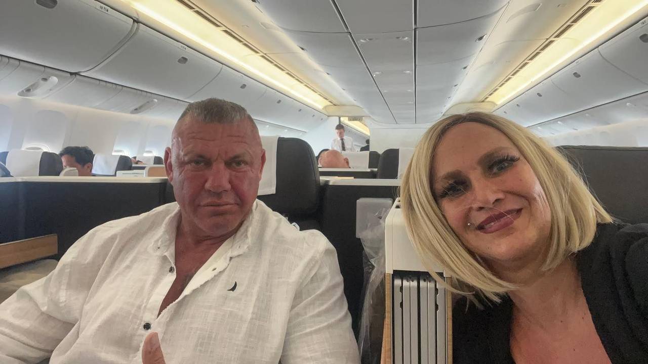 Caro und Andreas Robens sitzen im Flugzeug und schauen für ein Selfie in die Kamera.
