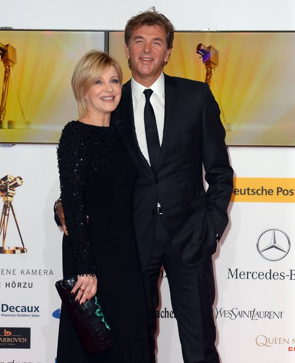 Carmen Nebel und Norbert Endlich posieren lächelnd in Gala-Kleidung auf dem roten Teppich der Goldenen Kamera