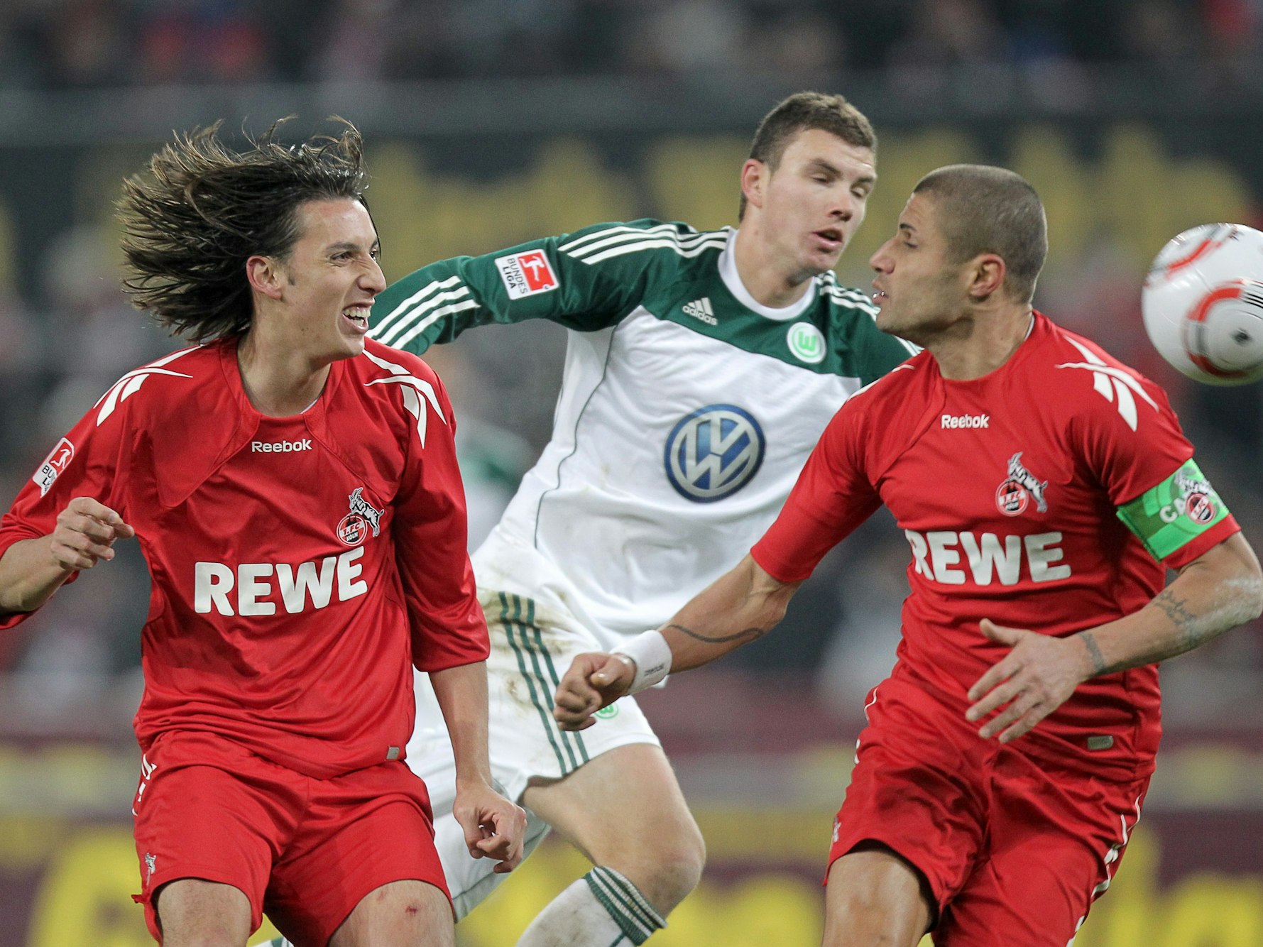 Die Kölner Pedro Geromel (l) und Youssef Mohamad (r) und der Wolfsburger Edin Dzeko (M) versuchen an den Ball zu kommen.